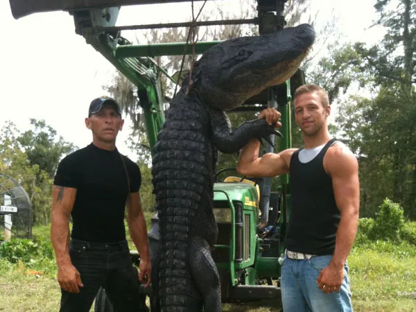 Two Swamp People alligator hunters holding up an alligator they caught
